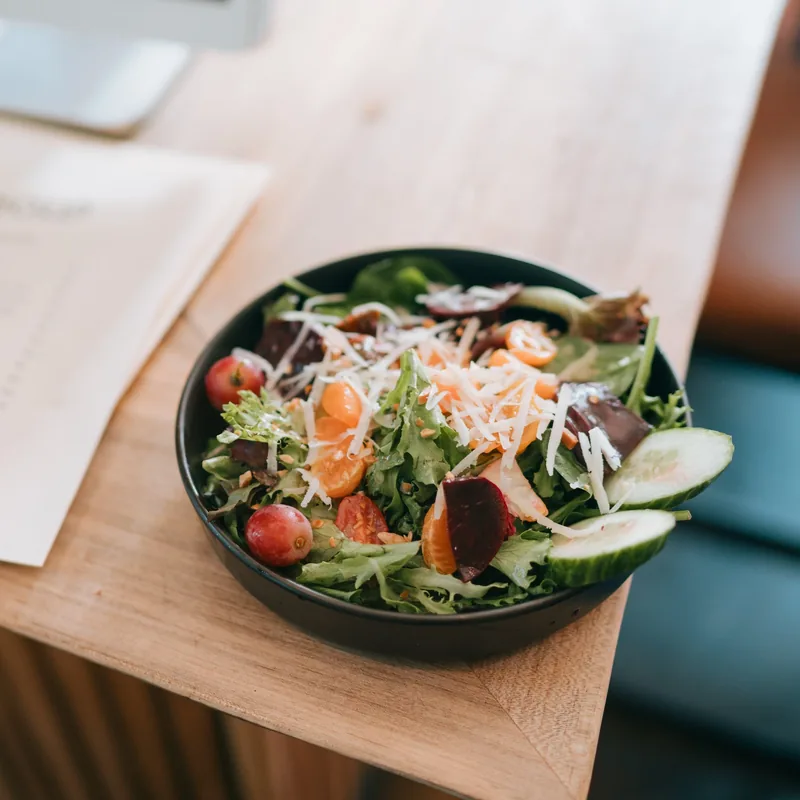 A bowl of greens with beets, tomato and shaved cheese